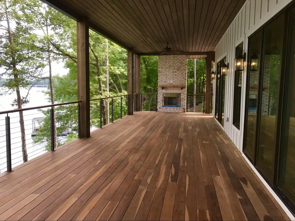 Covered wood deck overlooking a lake, with cable railing and a brick fireplace