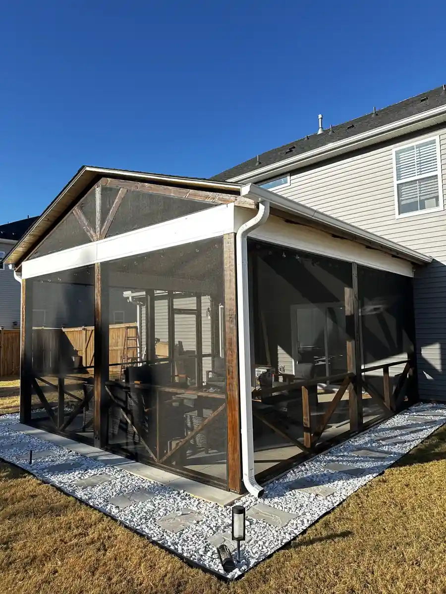 Ground-level screen porch with dark wood X-rail panels and a white gravel border