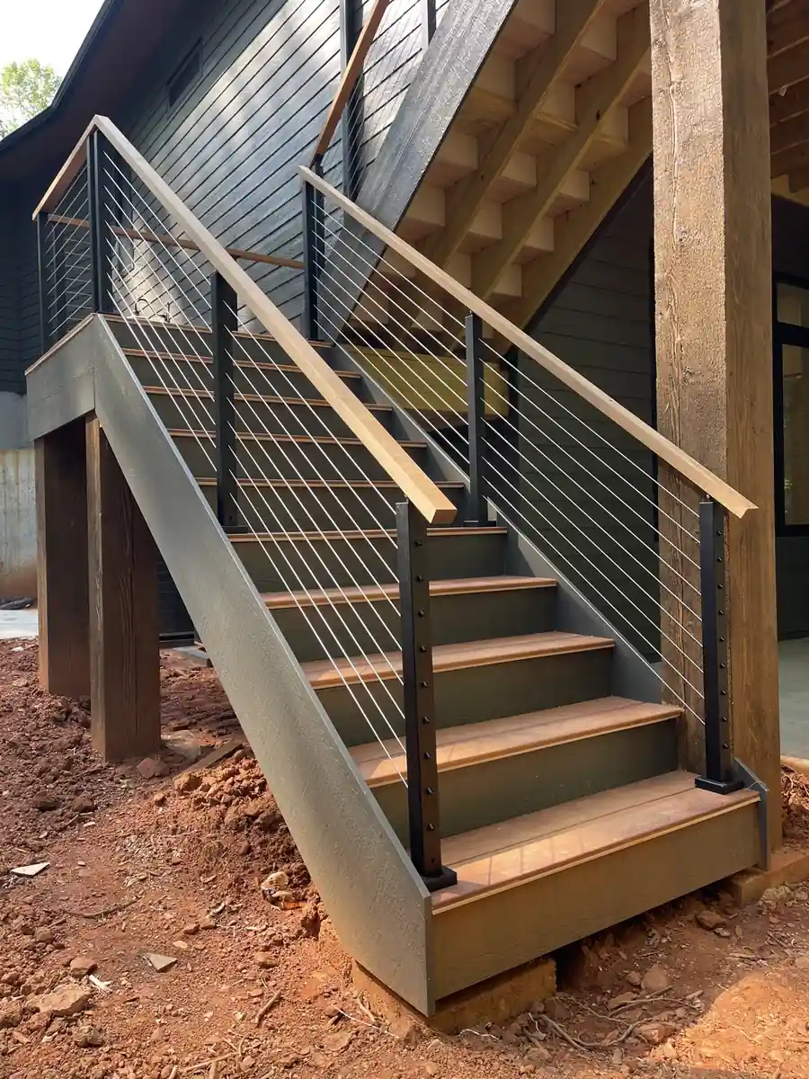 Cable railing with a wood top rail on exterior deck stairs of a dark-sided home