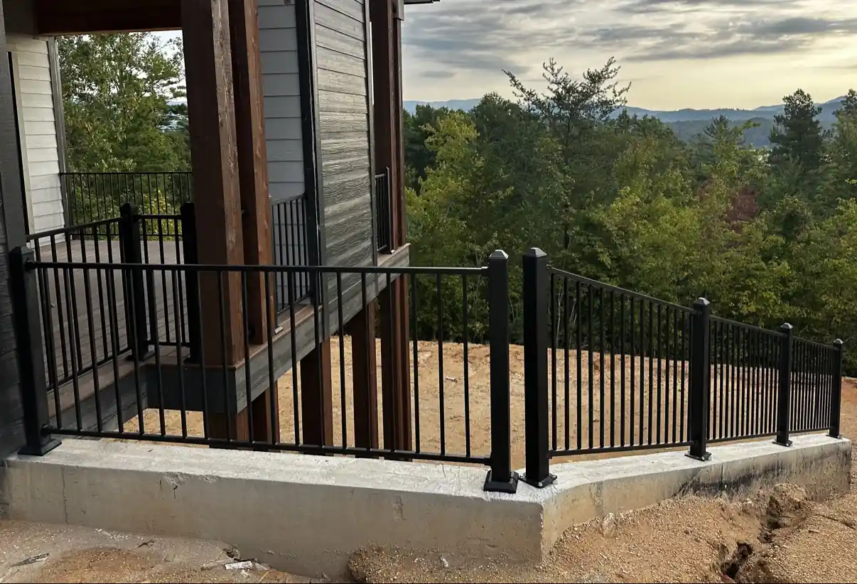 Black steel railing mounted on a concrete edge beside a deck, with trees and mountains behind