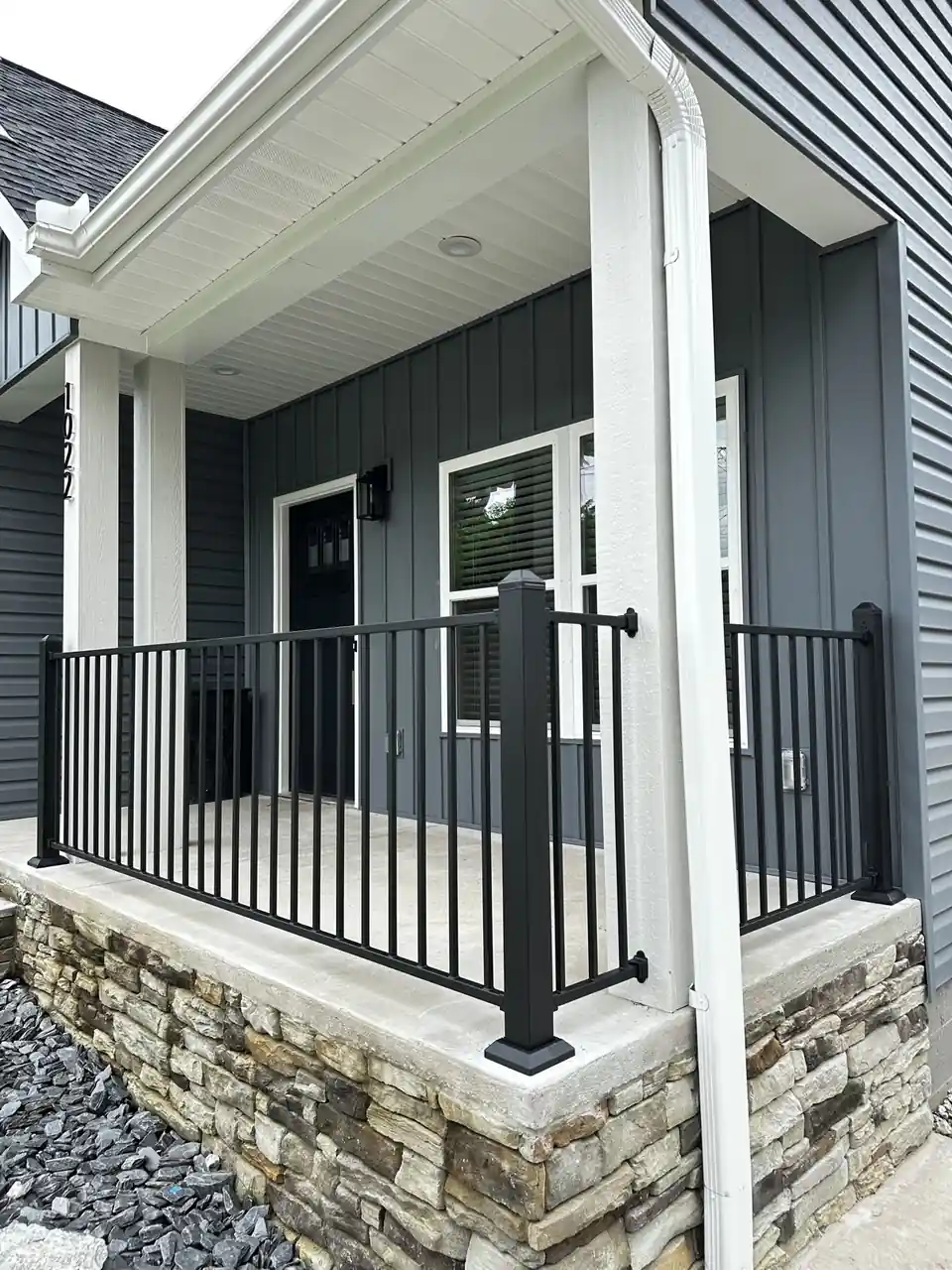 Black steel railing on a raised stone-front front porch of a dark grey home