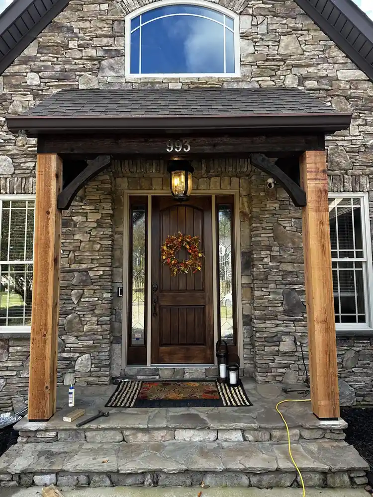 Stone home front entry with a timber-post porch, wood front door, and stone steps