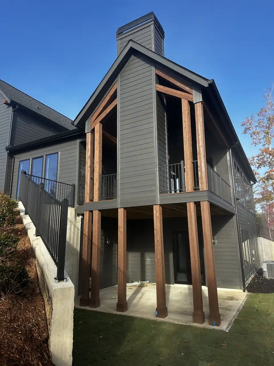 Dark grey home with a two-story timber-post porch and balcony over a concrete patio